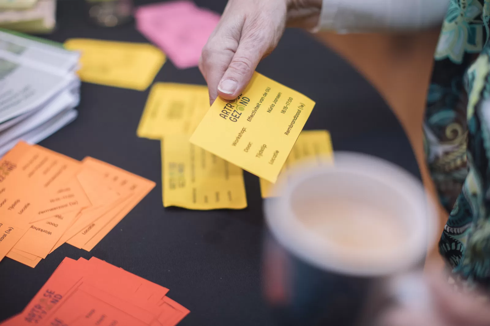 Tafel met gekleurde kaartjes met daarop de verschillende workshops, een hand pakt een geel kaartje vast
